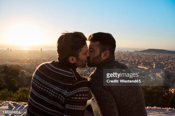 gay boyfriends kissing while sitting on observation point, bunkers del carmel, barcelona, spain - gay kiss stock-fotos und bilder