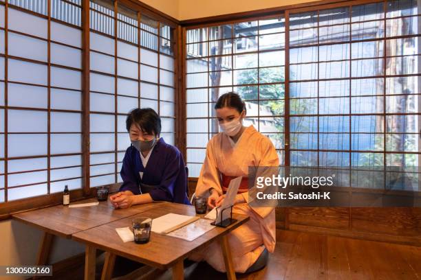 japanische frau und kaukasische frau in kimono mit schützender gesichtsmaske blick auf menü in traditionellen japanischen café - fersensitz stock-fotos und bilder