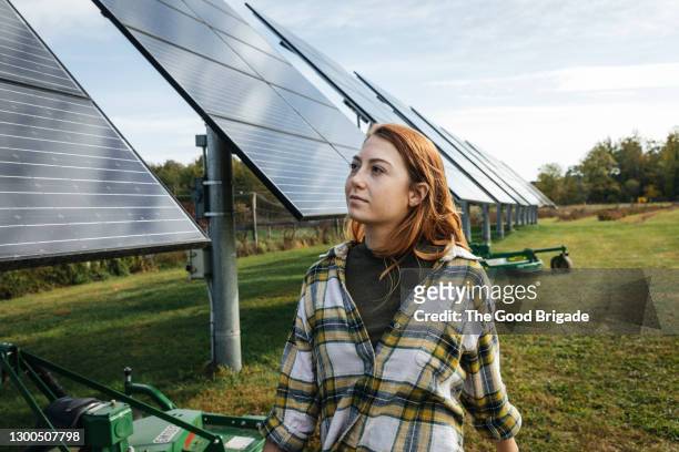 young woman looking at solar panels on farm - zonnecellen stockfoto's en -beelden