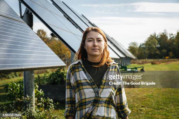 young woman standing in front of solar panels on farm - female farmer stock-fotos und bilder
