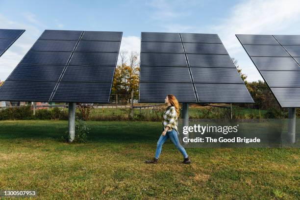 young woman walking next to solar panels on farm - green economy stock-fotos und bilder