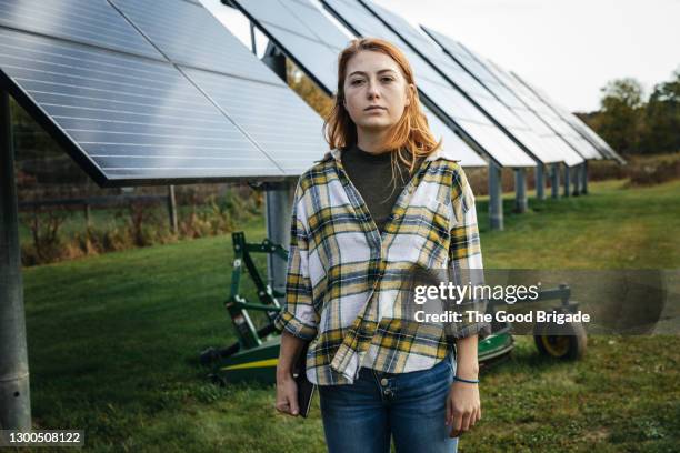 portrait of female farmer standing next to solar panels on farm - business sostenibile foto e immagini stock