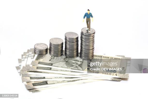 stack of coins and indian currency on white background - valuta indiana foto e immagini stock