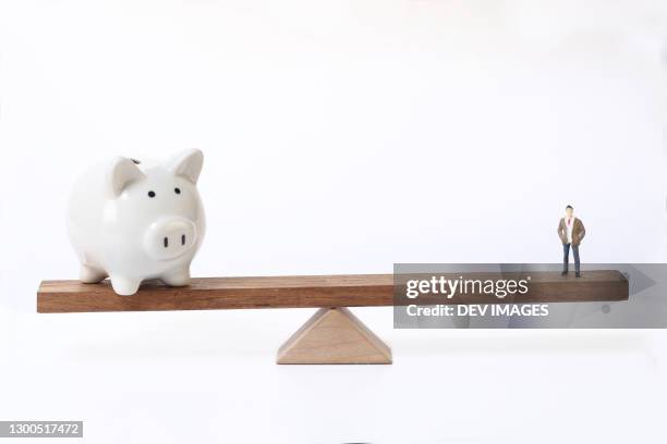 white pigyg bank and human figurine balancing on seesaw - income inequality stock pictures, royalty-free photos & images