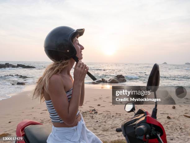la mujer se detiene en la playa local con su scooter, ajustando el casco - riding scooter fotografías e imágenes de stock