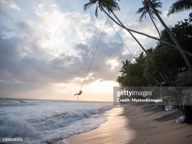 woman plays on rope swing above sea - rope swing stock pictures, royalty-free photos & images