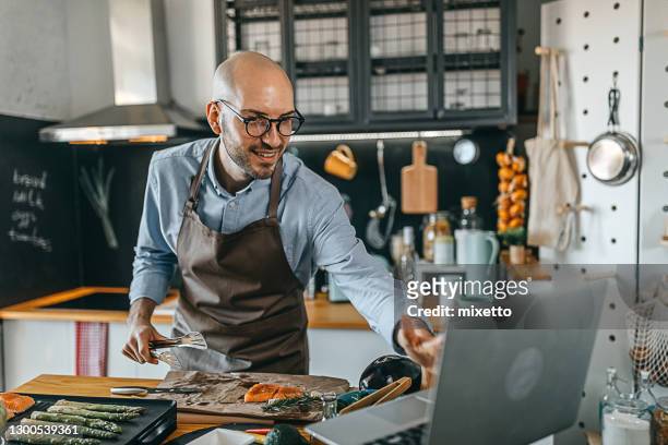 jeune homme apprenant à cuisiner tout en regardant des tutoriels dans internetlearning, - kitchen internet photos et images de collection