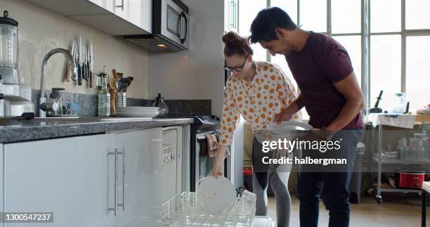 young couple loading dishwasher - loading dishwasher stock pictures, royalty-free photos & images