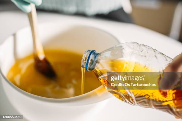 soap making at home - hand wearing a protective rubber glove stirring the liquid formed by water and sodium hydroxide mixture with a wooden spoon in a white pastic bowl - rubber bowl 個照片及圖片檔