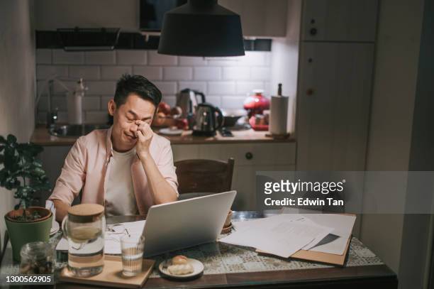 night overwork asian chinese male working late at home dining room emotional stress with his financial bill alone at night - emotional stress stock pictures, royalty-free photos & images