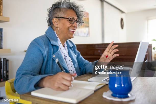 mature black woman working from home - 50s woman writing at table imagens e fotografias de stock