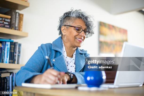 mature black woman working from home - 50s woman writing at table imagens e fotografias de stock