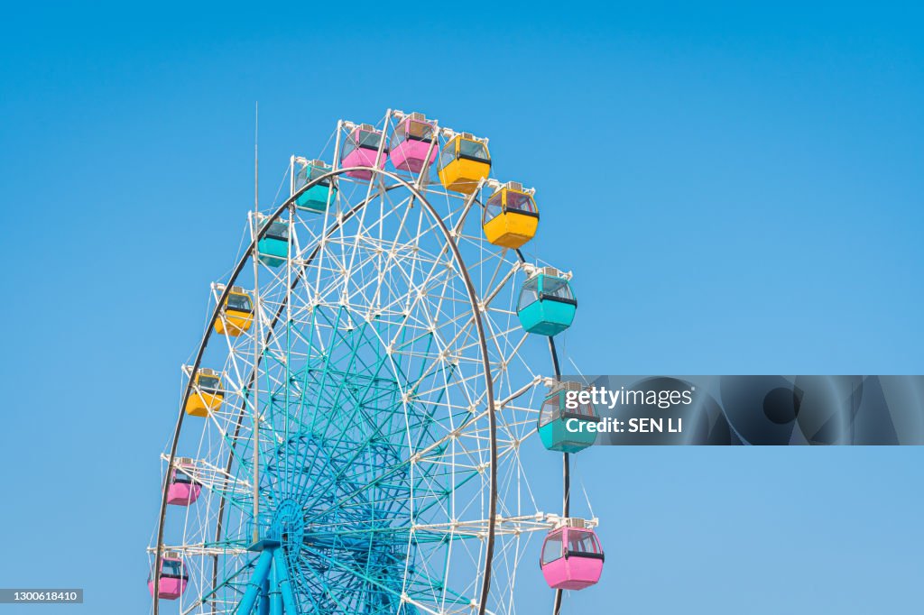 Colorful ferris wheel in an amusement park against blue sky