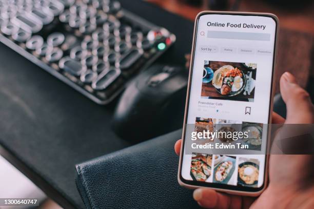 aplicación móvil de entrega de alimentos en línea que se muestra en la pantalla del teléfono inteligente sostener por las manos de hombre asiático en frente de pc de escritorio - food delivery fotografías e imágenes de stock