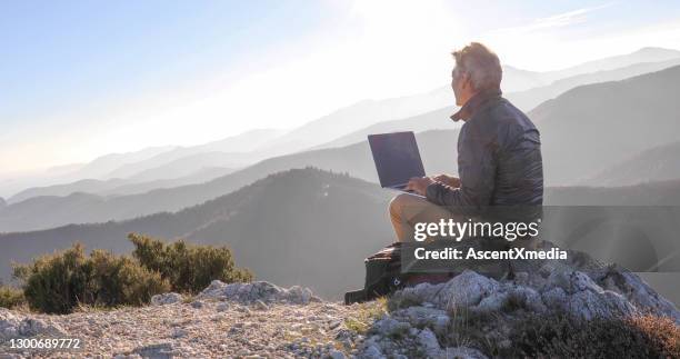 hombre maduro utiliza computadora en la cima de la montaña al amanecer - remote location fotografías e imágenes de stock