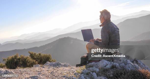 mature man uses computer on mountain top at dawn - desolate mountains stock pictures, royalty-free photos & images