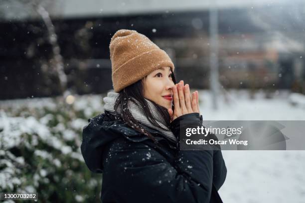 beautiful young asian woman warming her hands in the snow - winter coat fotografías e imágenes de stock