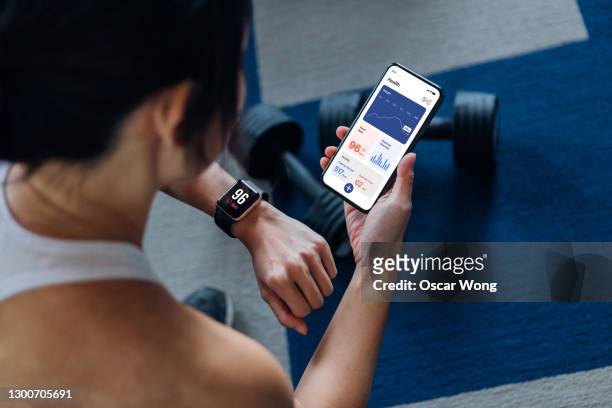over the shoulder view of young active woman using exercise tracking app on smartphone to monitor her training progress after exercising at home - applicazione mobile foto e immagini stock