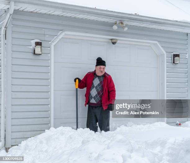 a tired senior man with a shovel takes a break when cleaning the snow in front of his garage. - old garage at home stock pictures, royalty-free photos & images