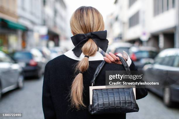 Low bubble ponytail hairstyle, a black bow hair clip by Chanel and a black and white bag by Chanel as a detail of influencer Gitta Banko during a...