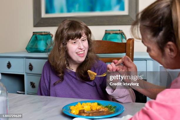 caretaker assists disabled young adult eating her dinner - autism adult stock pictures, royalty-free photos & images