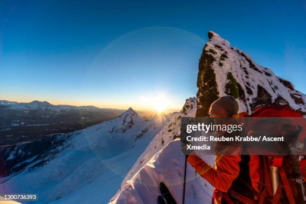 ski mountaineer ascends summit slope, mountains below - sundog stock pictures, royalty-free photos & images