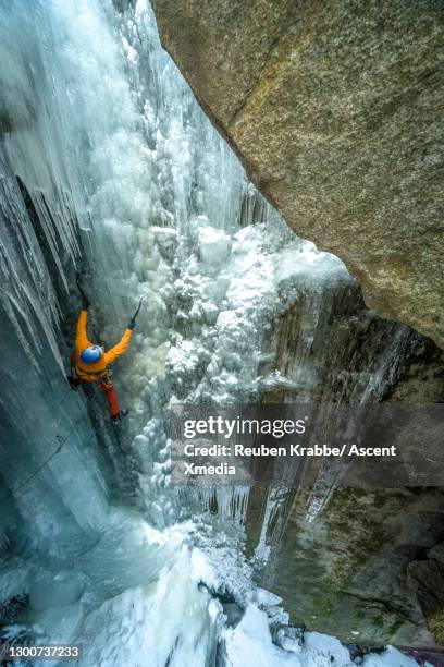 ice climber ascends vertical frozen waterfall - ice pick stock-fotos und bilder