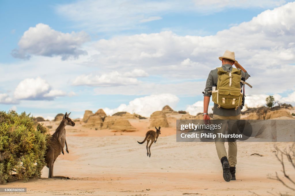 Young man walking in arid desert landscape with photography backpack on an adventure in outback Australia
