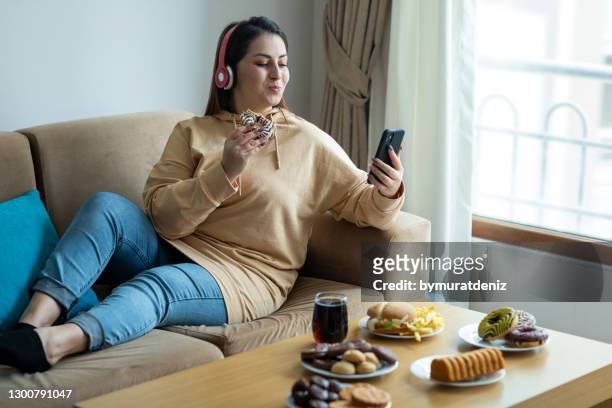 ung kvinna äter skräpmat hemma - unhealthy living bildbanksfoton och bilder