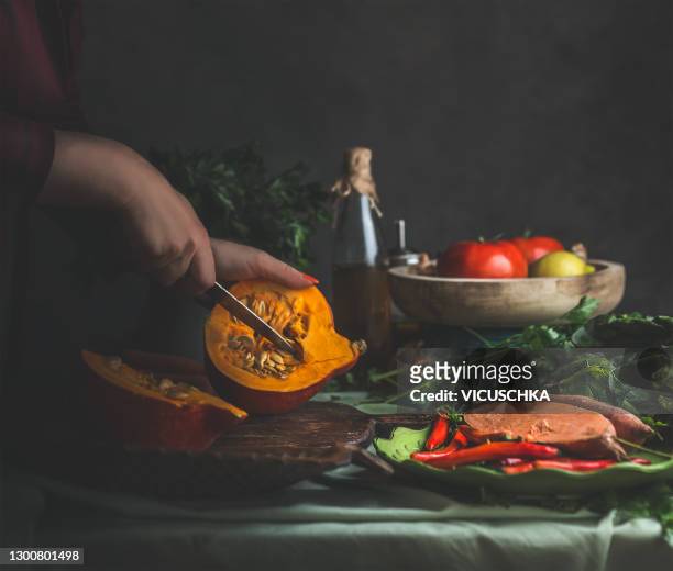 woman hands preparing hokkaido pumpkin on rustic kitchen table with other healthy vegetarian ingredients. dark. - hokaido pumpkin stock pictures, royalty-free photos & images