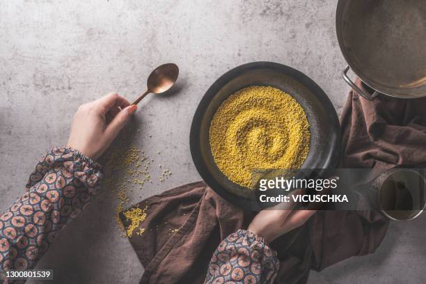 woman hands holding bowl with uncooked millet on dark concrete background. - mijo fotografías e imágenes de stock