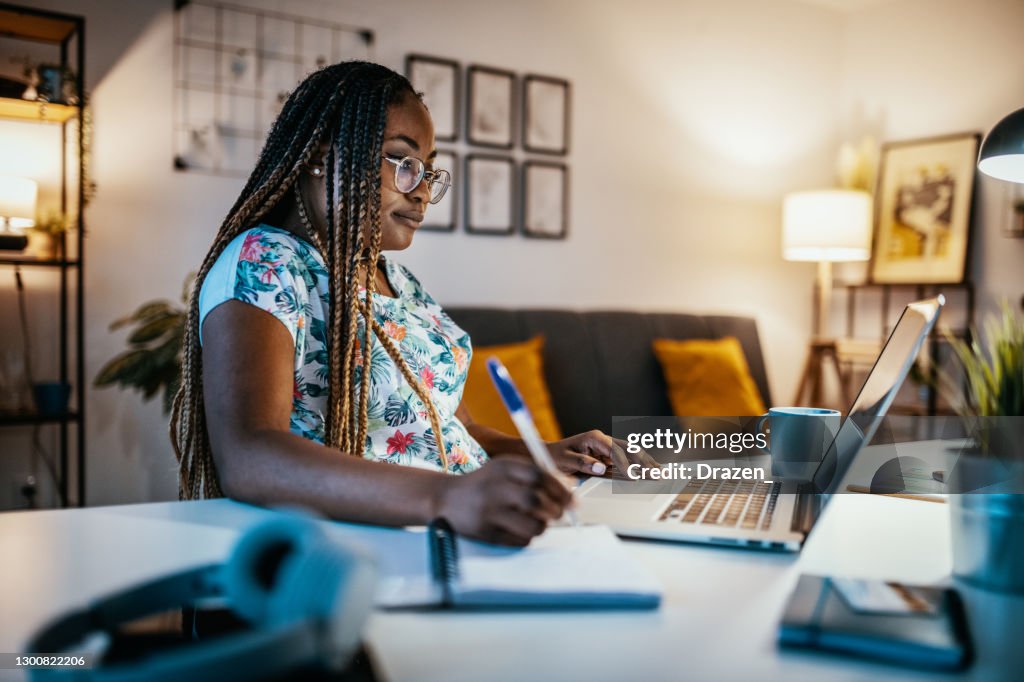 African American female student studying from home and taking notes from professor