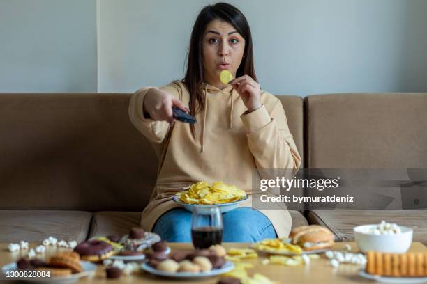 de te zware vrouw zit op de bank met junkfood - ongezond leven stockfoto's en -beelden