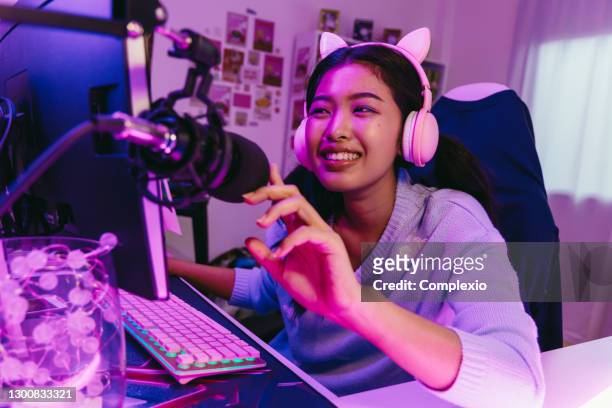 オンラインビデオゲームをプレイマイクとかわいいヘッドセットで興奮し、笑顔のゲーマーの女の子。自宅でパーソナルコンピュータで選手や聴衆と話す若いアジアの女性 - very young asian girls ストックフォトと画像