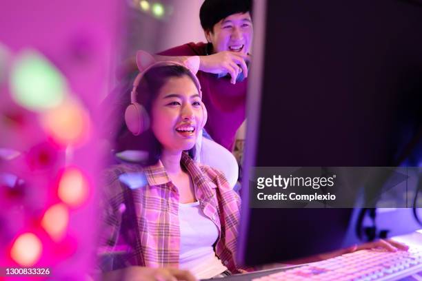 若い魅力的なアジアの女性は、後ろに彼女のボーイフレンドと彼女のスタジオオフィスでビデオゲームをプレイ。プロのデザインスタジオで同じワークステーションの前で働くカップルのサ� - media night ストックフォトと画像