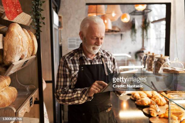 senior baker man in bakery shop using digital tablet - french boulangerie stock pictures, royalty-free photos & images