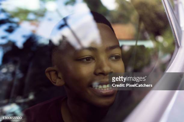 young african boy looking out car window reflections on glass - african car stock pictures, royalty-free photos & images