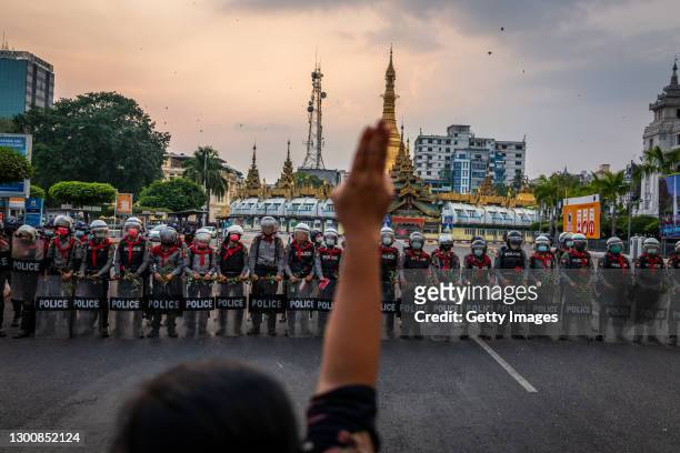 Protester makes a three-finger salute in front of a row of riot police, who are holding roses given to them by protesters, on February 06, 2021 in...
