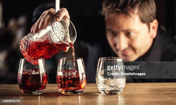 skilled bartender pours negroni short drink cocktail into three glasses. - accompagnement professionnel photos et images de collection