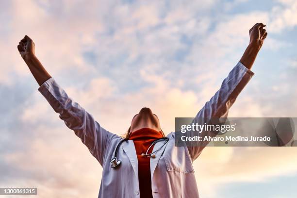female doctor raising her arms in victory. concept of medicine and fight against coronavirus. - reconocimiento fotografías e imágenes de stock