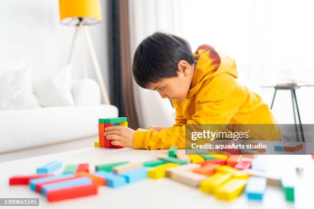 little cute kid is playing colorful wooden blocks game home in the living room.  having fun and learning creativity. - jenga stock pictures, royalty-free photos & images