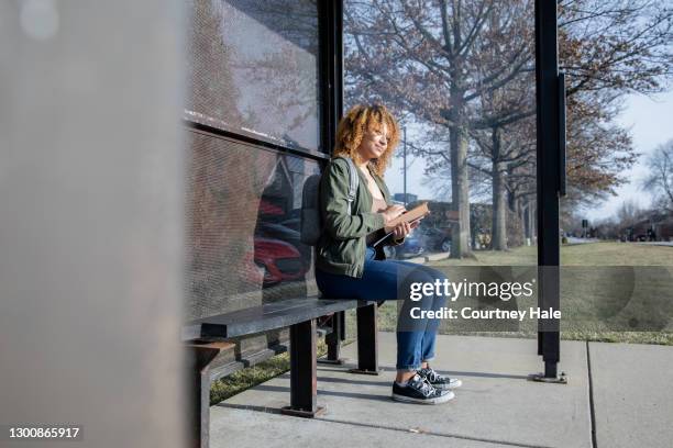 young black woman is college student waiting for public transportation near campus on her way to university class - waiting bus stock pictures, royalty-free photos & images