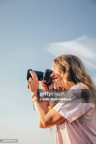 attractive young woman photographer with photo camera, taking photos and having fun on the beach in sunny weather. - beach photos stock-fotos und bilder