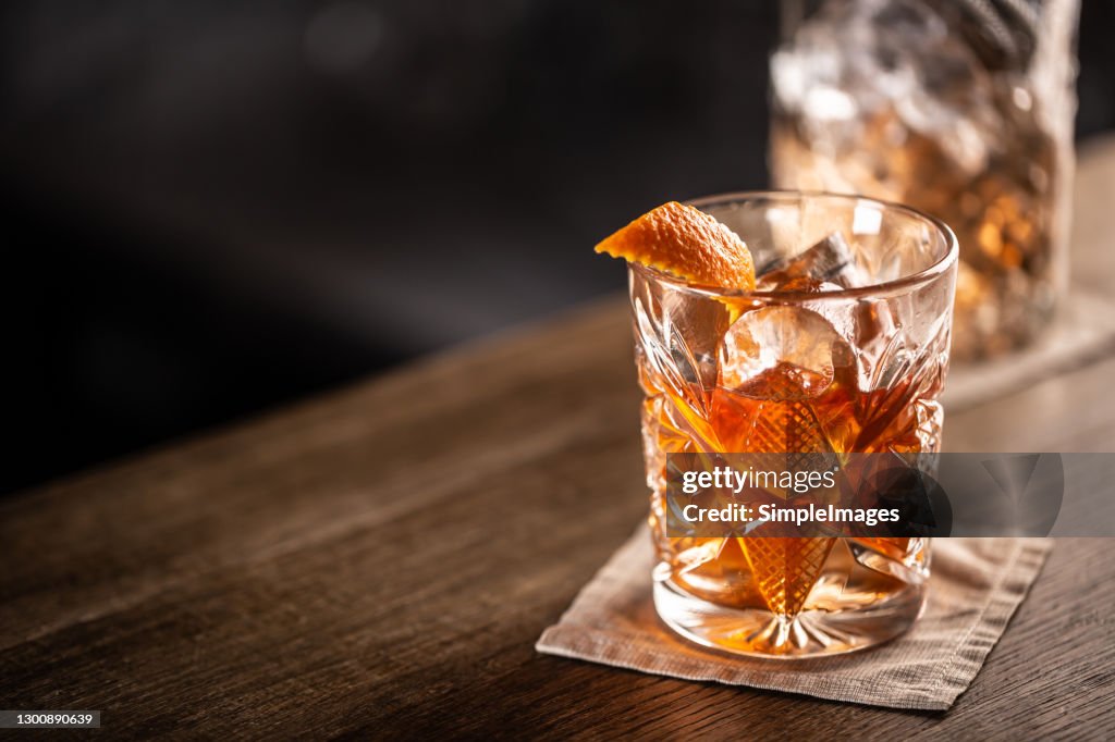 Old fashioned whiskey drink on ice with orange zest garnish.