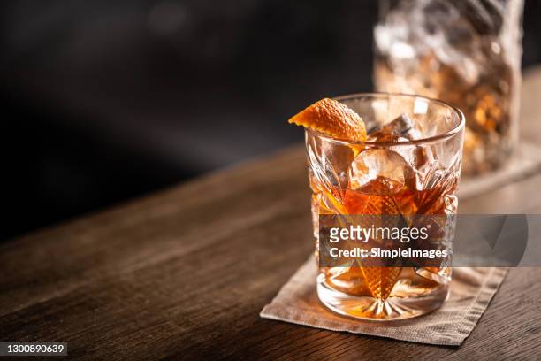 old fashioned whiskey drink on ice with orange zest garnish. - refreshment photos et images de collection