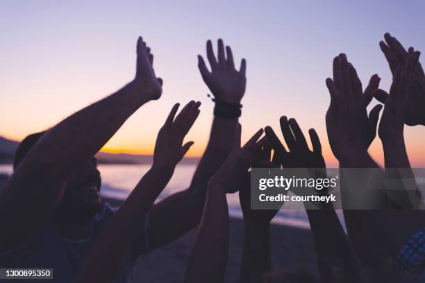 silueta de un grupo de personas con las manos levantadas al atardecer o al amanecer. - religion diversity fotografías e imágenes de stock