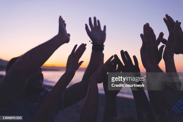 silhouette of a group of people with their hands raised at sunset or sunrise. - arms raised stock pictures, royalty-free photos & images