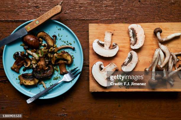 still life of cooked and raw mushrooms on old brown table - champignon stockfoto's en -beelden
