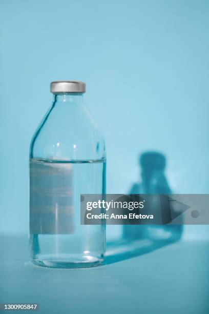 bottle with saline on blue background with shadow and illuminating reflections. covid-19 fighting concept - flebo salina foto e immagini stock