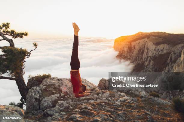 man practicing hatha yoga in headstand (salamba shirshasana) position in mountains with amazing view of low clouds at sunset - shirshasana stock pictures, royalty-free photos & images